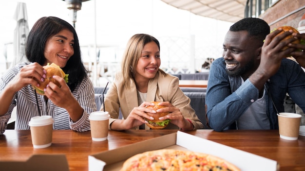 Amigos de tiro medio en la mesa con hamburguesas