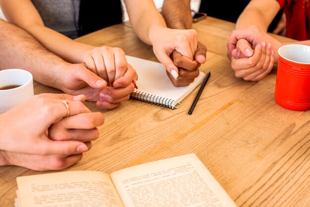 Amigos tomados de la mano cerca de papelería y tazas de café sobre el escritorio de madera