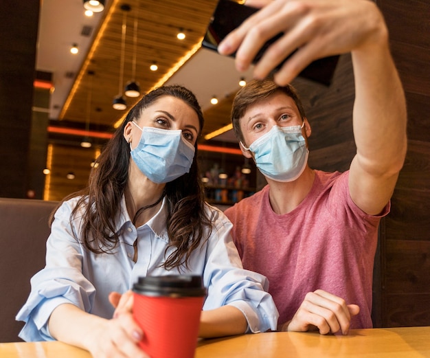 Amigos tomando un selfie en un restaurante con una máscara médica