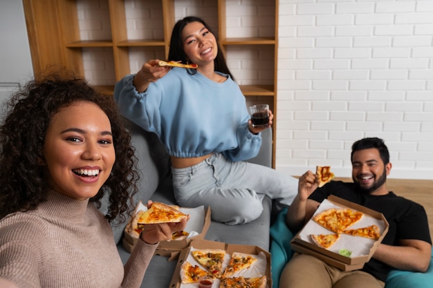 Amigos tomándose un selfie juntos mientras comen pizza