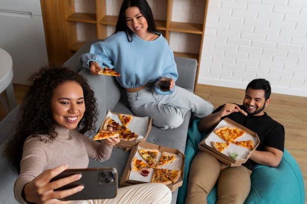 Amigos tomándose un selfie juntos mientras comen pizza