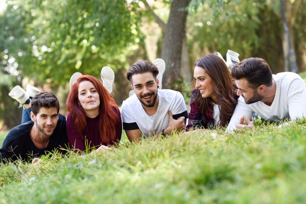 Amigos tumbados boca abajo en el césped de un parque sonriendo