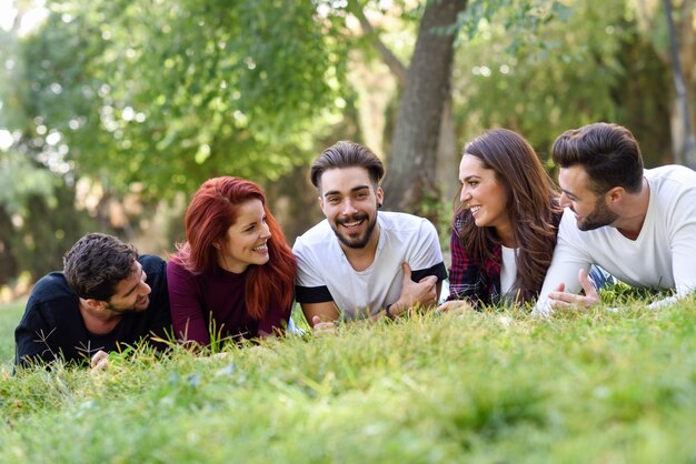 Amigos tumbados boca abajo en el césped de un parque sonriendo