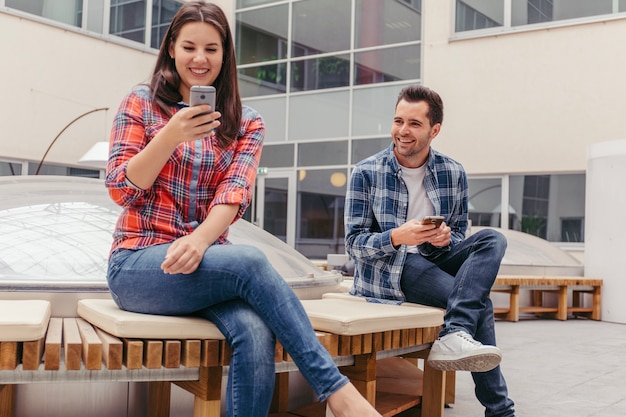 Amigos usando teléfonos y sentado en el banco