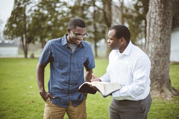 Amigos varones afroamericanos de pie en el parque y discutiendo la Biblia