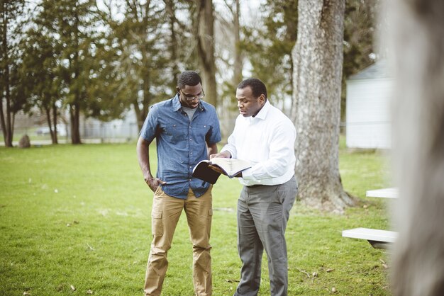 Amigos varones afroamericanos de pie en el parque y discutiendo la Biblia
