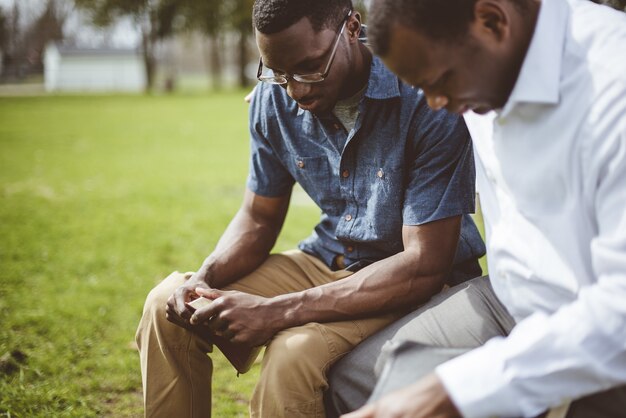 Amigos varones afroamericanos sentados y orando con los ojos cerrados y la Biblia en sus manos