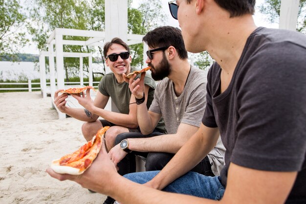 Amigos varones disfrutando de pizza en la playa