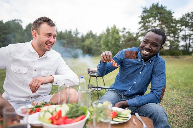 Amigos varones sonrientes comiendo barbacoa al aire libre