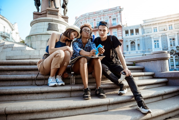 Amigos viajeros con mochilas sonriendo, haciendo selfie, sentados cerca de la vista.