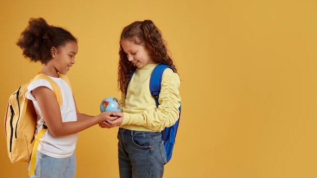 Foto gratuita amistad de la escuela de niñas sosteniendo un espacio de copia de globo terráqueo