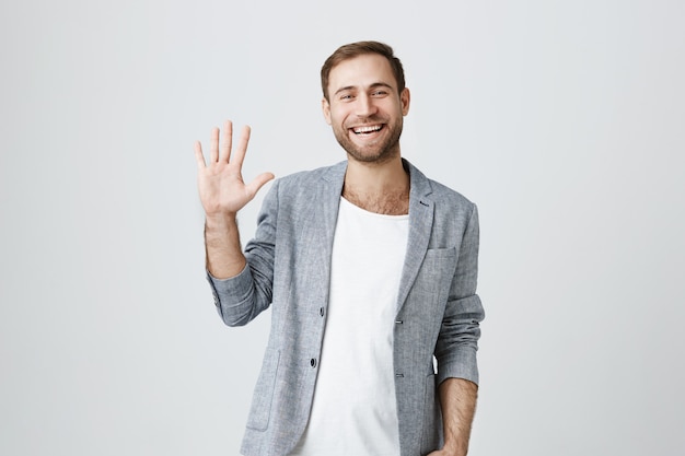 Amistoso chico guapo sonriente saludando con la mano, saluda