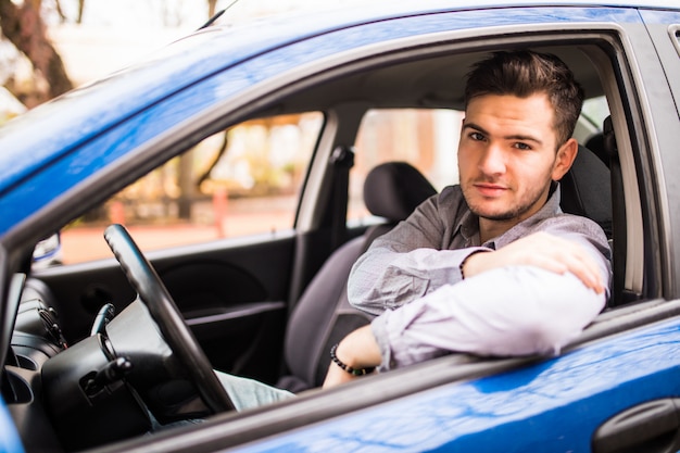 Amo mi carro. Apuesto joven conducía su automóvil y sonriendo a la cámara