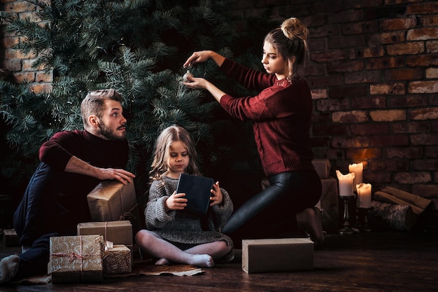 Amor, familia, Navidad. Una familia atractiva decora el árbol de Navidad, rodeada de regalos en casa.