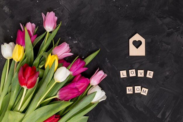 Amor; mamá; Alfabeto en bloques de madera con forma de corazón y coloridas flores de tulipán sobre fondo negro