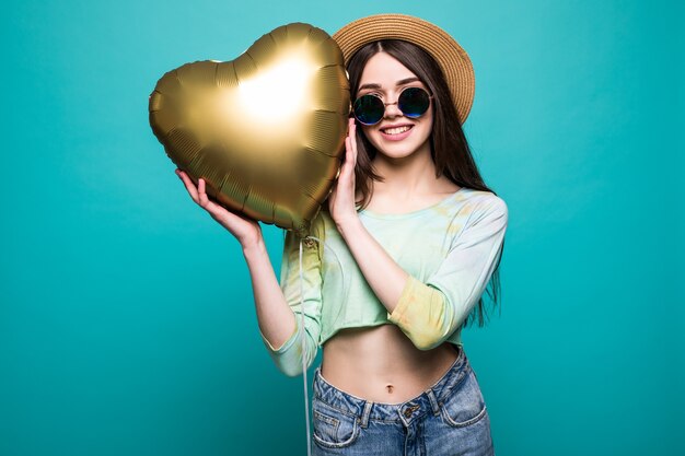 Amor mujer sonriente sosteniendo globo en forma de corazón de oro. Linda hermosa joven enamorada aislada en verde