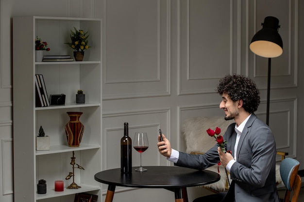 Amor virtual guapo chico lindo en traje con vino en una cita telefónica a distancia con flores