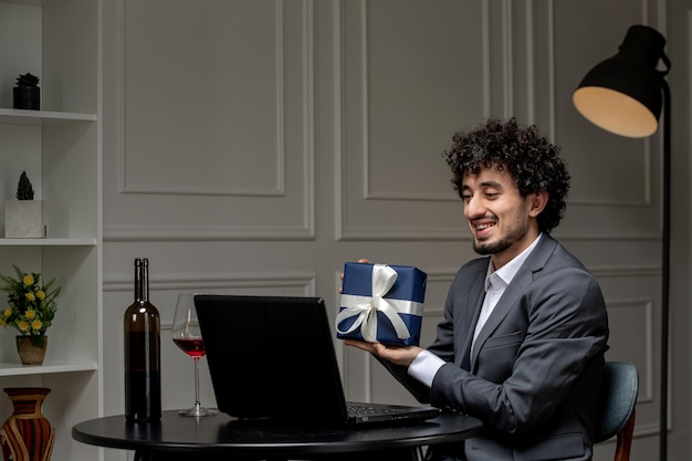 Amor virtual guapo chico lindo en traje con vino en una fecha de computadora a distancia con caja de regalo