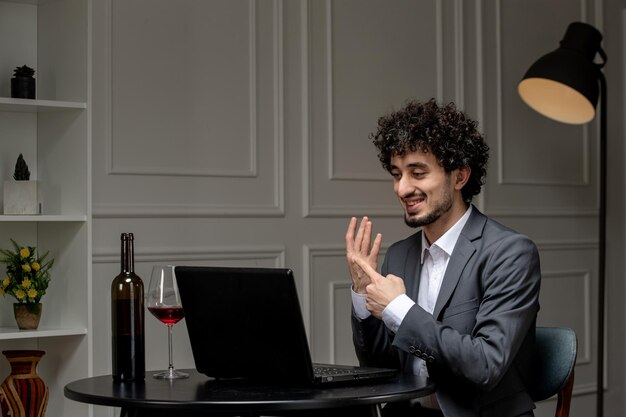 Amor virtual guapo chico lindo en traje con vino en una fecha de computadora a distancia que muestra el anillo en el dedo