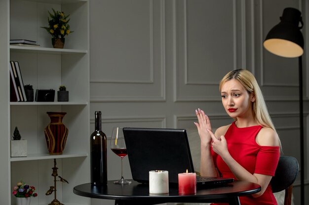 Amor virtual linda chica rubia con vestido rojo en una cita a distancia con vino en el dedo