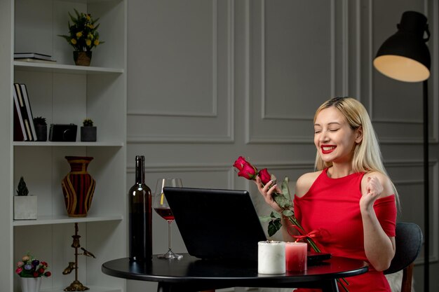Amor virtual linda chica rubia en vestido rojo en cita a distancia con vino emocionado