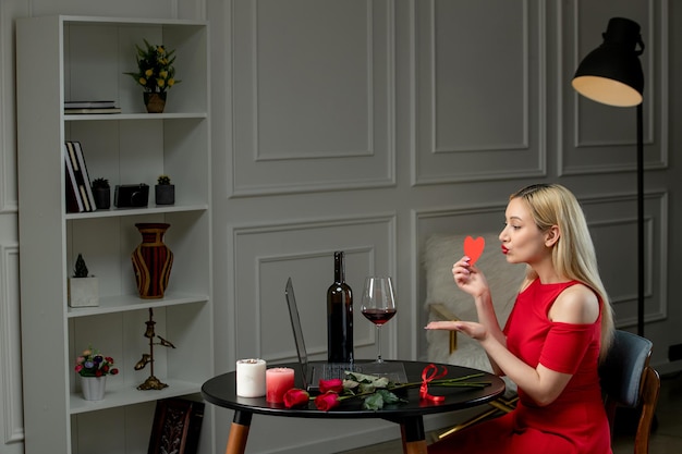 Amor virtual linda chica rubia con vestido rojo en una cita a distancia con vino y velas besándose