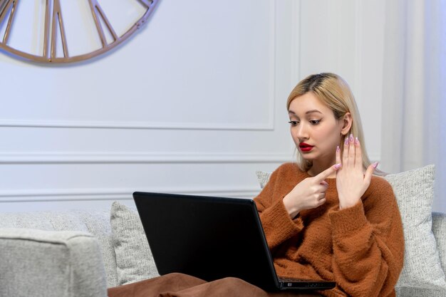 Amor virtual linda jovencita rubia en un suéter acogedor en la fecha de distancia de la computadora señalando con el dedo