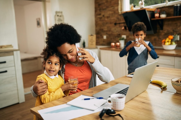 Amorosa madre afroamericana hablando por teléfono mientras trabaja en casa
