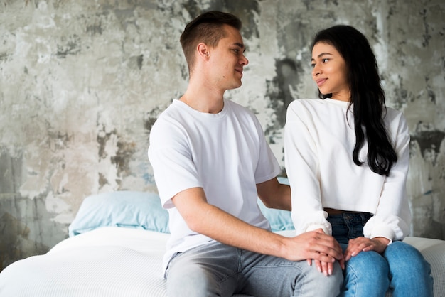 Amorosa pareja casual sentado en la cama y mirando a los ojos