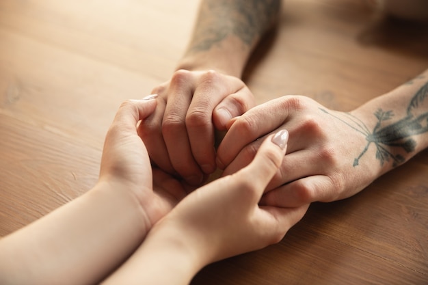 Amorosa pareja caucásica cogidos de la mano de cerca en la pared de madera.