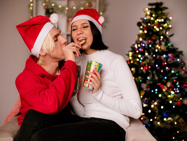 Amorosa pareja joven en casa en la época de Navidad con sombrero de santa sentado