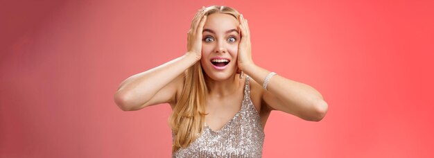 Amusado sorprendido emocionado joven rubia atractiva mujer en plata brillante vestido elegante sostener la cabeza