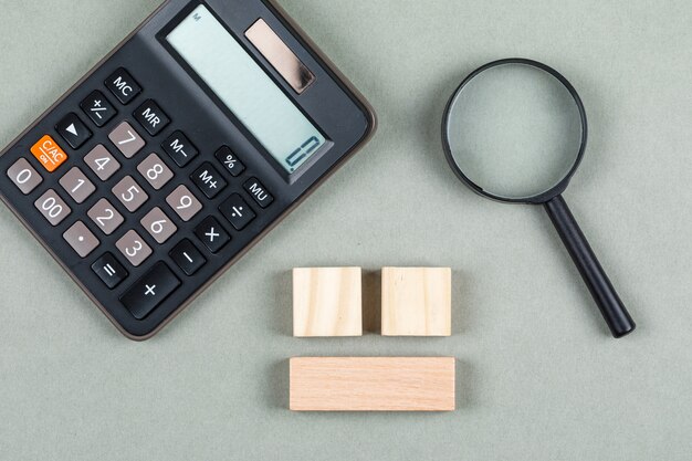 Análisis financiero y concepto de contabilidad con lupa, bloques de madera, calculadora en la vista superior de fondo gris. imagen horizontal