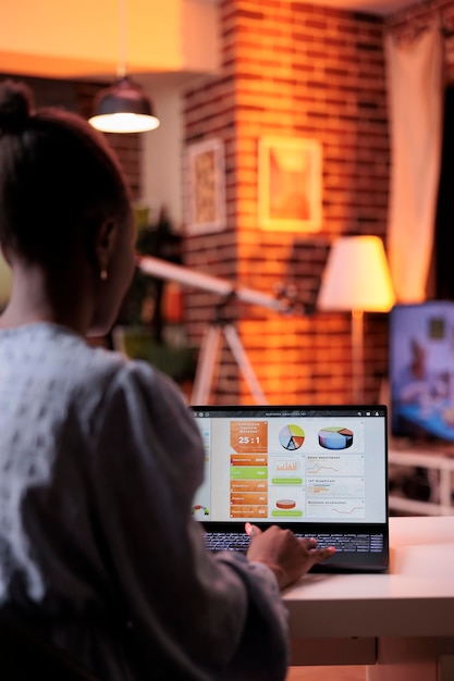 Foto gratuita analista de negocios femenina mirando diagramas y gráficos circulares en la pantalla de un portátil en una oficina doméstica moderna con una hermosa y cálida luz de puesta de sol. trabajador corporativo remoto que analiza los datos de resultados de investigación de la empresa