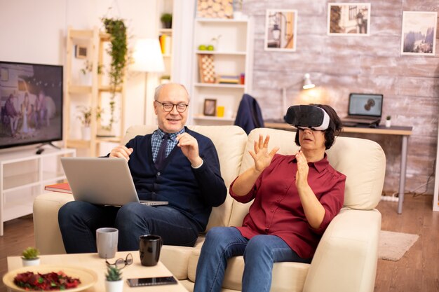 Anciana anciana jubilada de unos 60 años experimentando la realidad virtual por primera vez en su acogedor apartamento