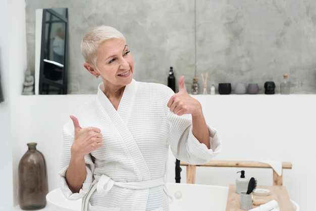 Anciana en bata de baño sonriendo y dando pulgares arriba