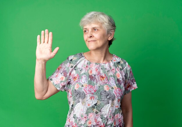 Anciana complacida levanta la mano mirando al lado aislado en la pared verde