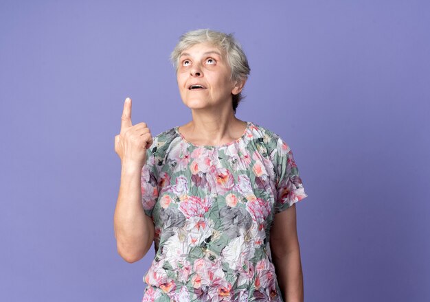Anciana complacida señala y mira hacia arriba aislado en la pared púrpura