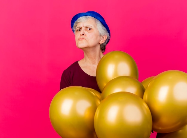 Anciana despistada con sombrero de fiesta se encuentra con globos de helio en rosa