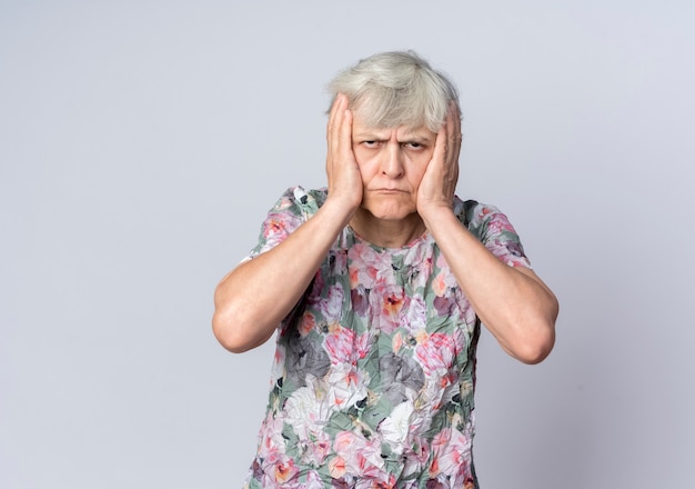 Anciana disgustada sostiene la cabeza con las dos manos aisladas en la pared blanca
