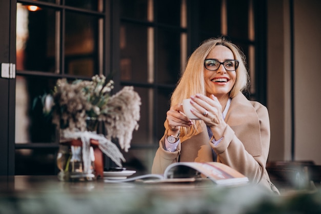 Anciana empresaria en un abrigo sentado afuera de un café y leyendo una revista