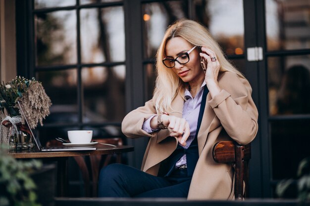 Anciana empresaria hablando por teléfono y sentado afuera del café