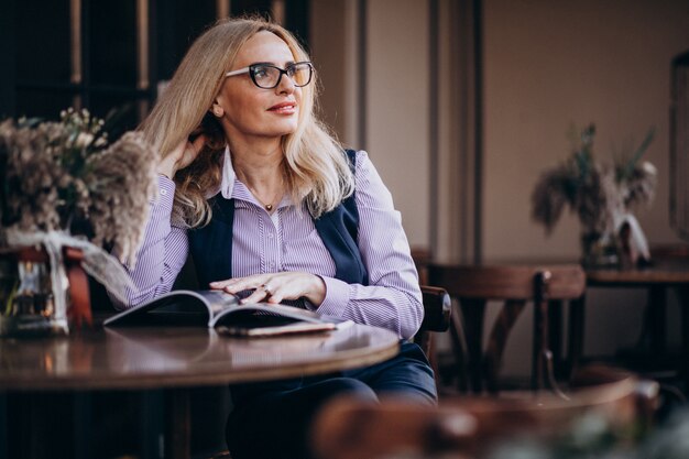 Anciana empresaria sentado afuera del café y leyendo una revista