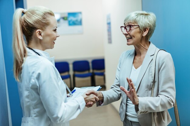 Una anciana feliz estrechándole la mano a un médico mientras hablaba con ella en el pasillo del hospital