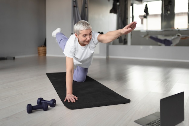 Anciana haciendo yoga en una estera de yoga en el gimnasio