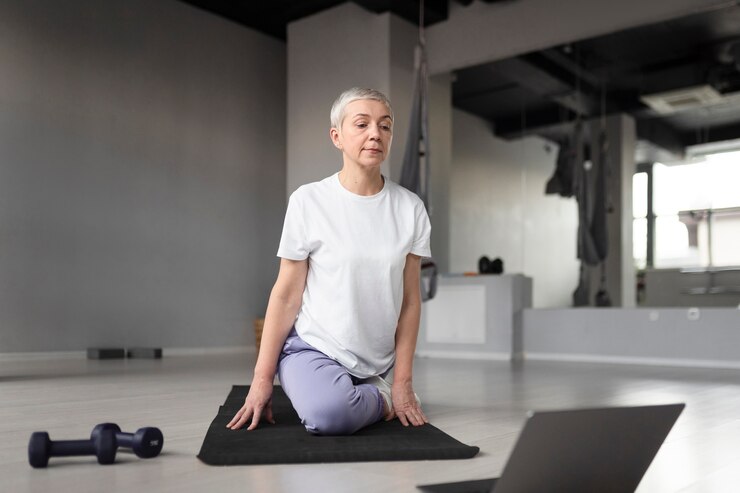 Anciana haciendo yoga en una estera de yoga en el gimnasio