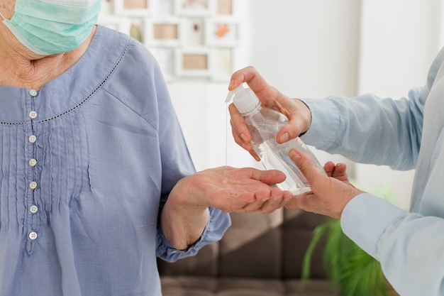 Anciana con máscara médica desinfectando su mano