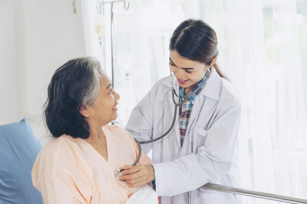 Anciana sonriendo con médico y visitando paciente mujer senior en sala de hospital