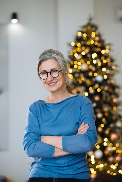 Anciana sonriendo y mirando a cámara en el fondo del árbol de Navidad