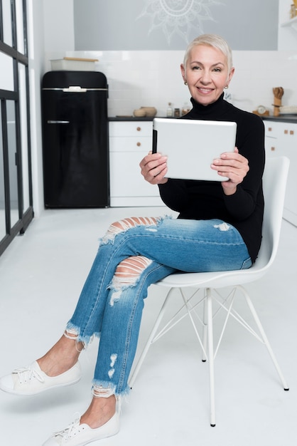 Anciana sonriendo y posando con tableta en la cocina